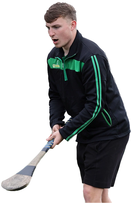 Young man playing hurling in black and green sportswear, holding a hurley stick, ready to hit the sliotar.