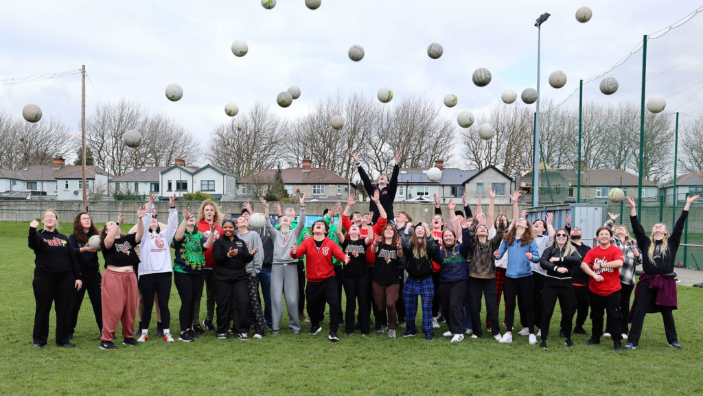 Group of people at a sports field joyfully tossing balls into the air, celebrating teamwork and outdoor fun.