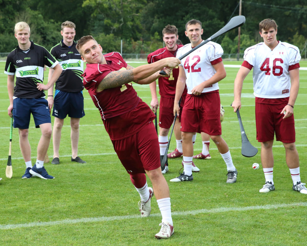 Athletes practicing hurling on a field, wearing numbered jerseys and using hurleys.