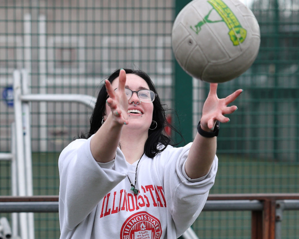 Person in a white sweater catching a volleyball outdoors on a court.