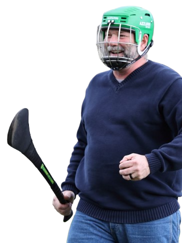 Man wearing a green helmet holding a hurley stick, dressed casually in a navy sweater and jeans.