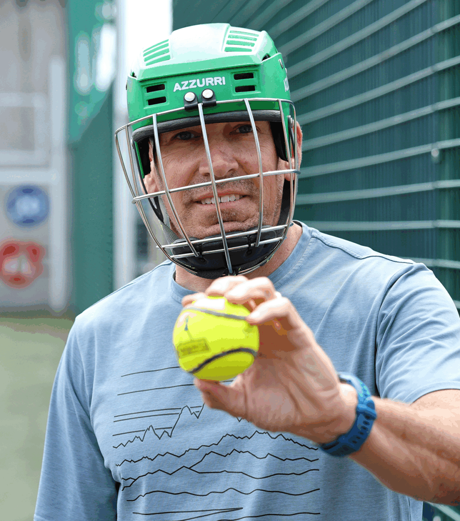 Man in green helmet holding a tennis ball on a sports field.