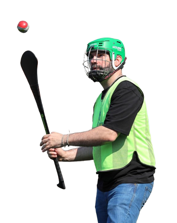 Hurling player in green helmet and vest practicing with hurley and sliotar in action.