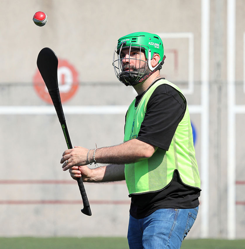 Man playing hurling, wearing a green helmet and vest, focusing on incoming sliotar.