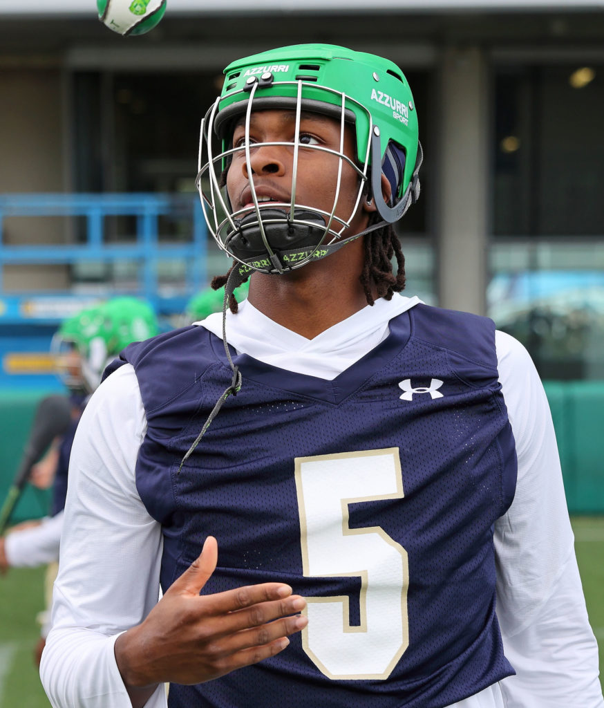GAA player in green helmet and jersey number 5 catches a ball during practice on the field.