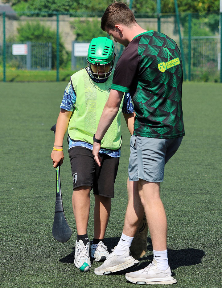 Coach instructing a young player during a Gaelic games training session on a sunny field.