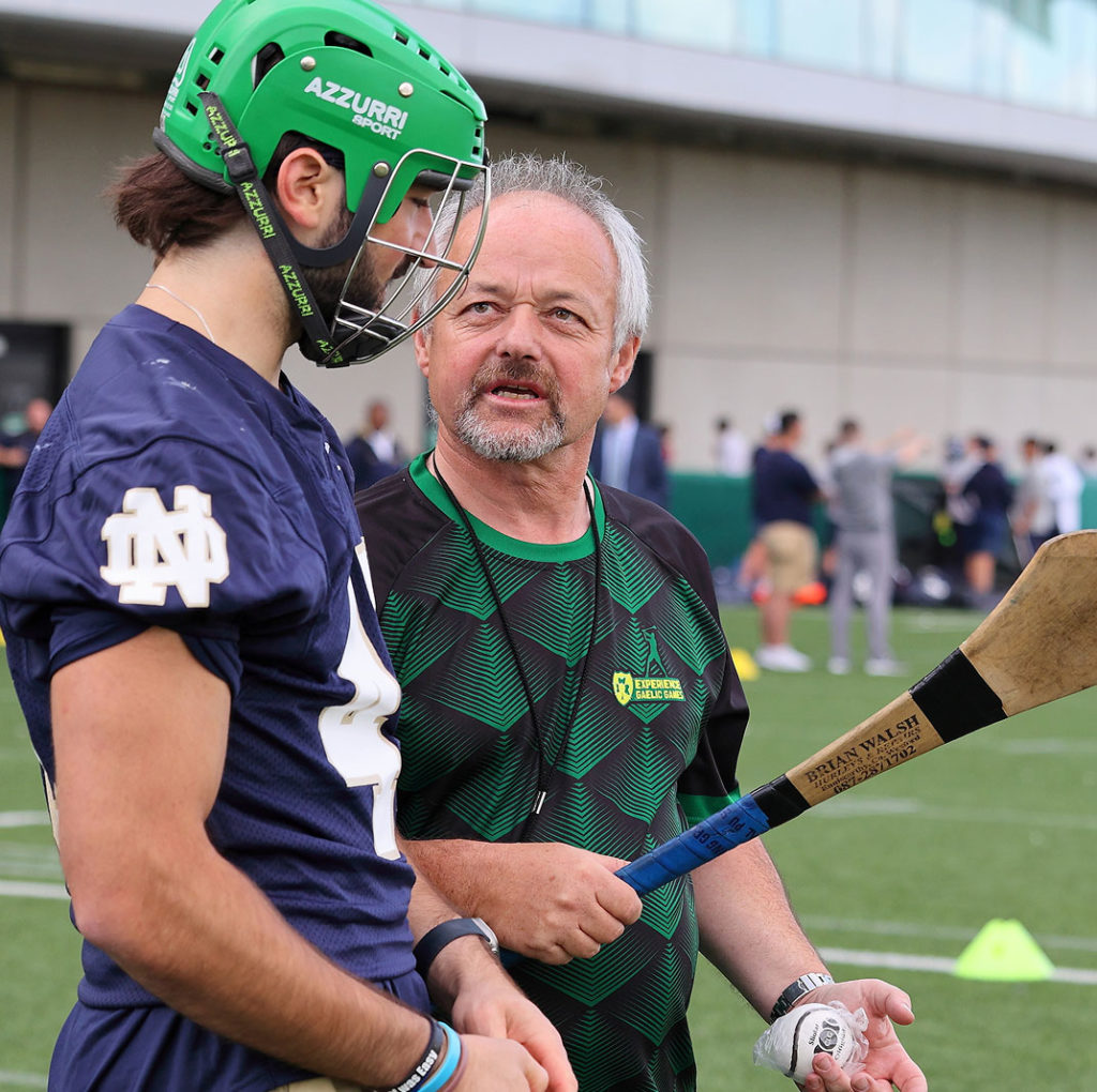 Coach discussing strategy with athlete in green helmet during outdoor sports practice.