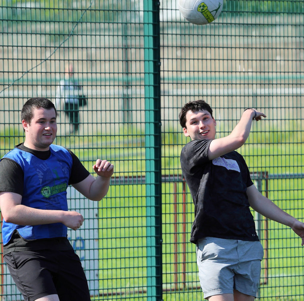 Two young men playing soccer, one heading a ball on a sunny outdoor court.