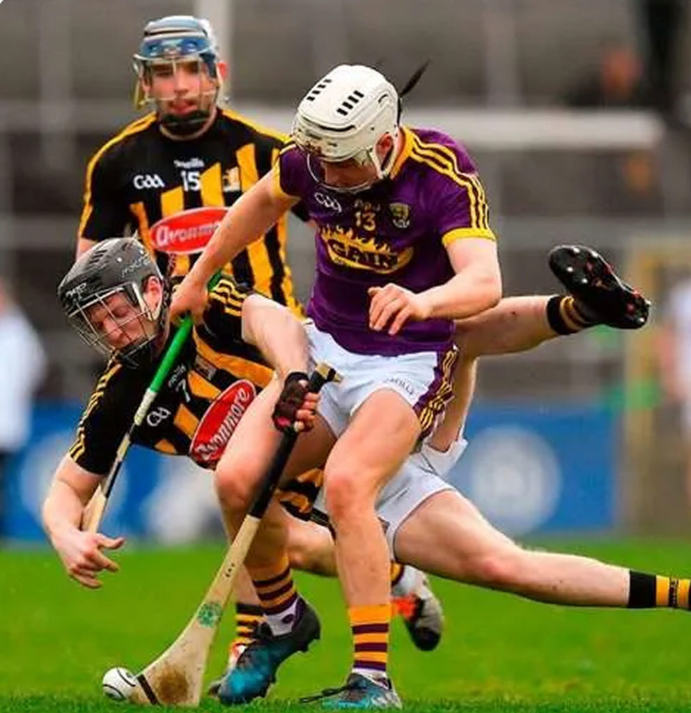 Hurling players in action during a competitive match, wearing helmets and team jerseys, competing for the ball.