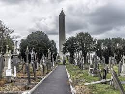 Historic cemetery with stone tombs and obelisk, framed by cloudy sky and trees, evokes serenity and timelessness.