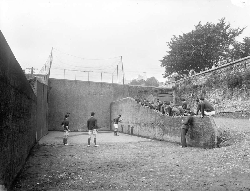 Historic handball game with players and spectators in a walled court, showcasing early 20th-century sports culture.