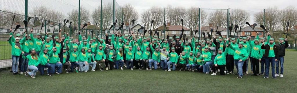 Group of people in green hoodies holding sticks on a sports field, celebrating teamwork and unity.