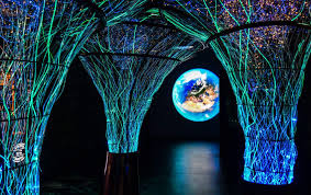 Futuristic art installation with illuminated structures and a glowing Earth globe in the background, surrounded by vibrant lights.