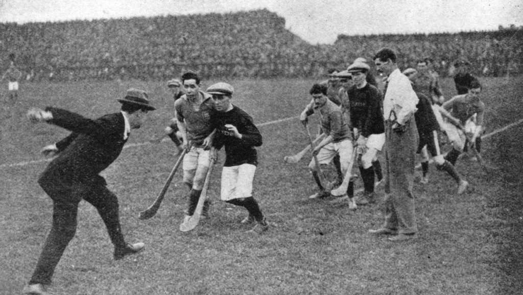 Historical hurling match with players in action on a grass field, vintage black and white photo.