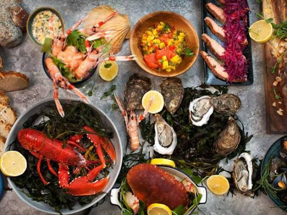 Assorted seafood platter with lobster, prawns, oysters, and diverse garnishes on a rustic table setting.
