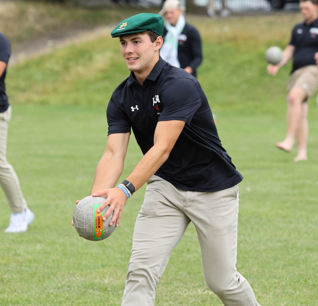 Young man playing touch rugby on grass, wearing a green cap and black shirt.