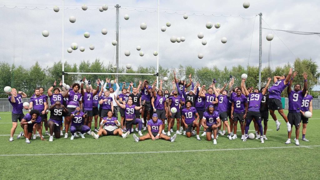 Football team in purple jerseys celebrating with tossed balls on a field. Team spirit and joy captured in action.