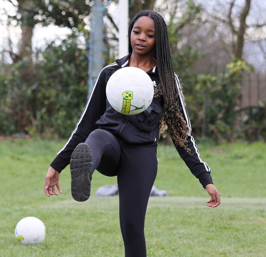 Young woman juggling a soccer ball on grass in athletic gear, showcasing soccer skills in an outdoor setting.