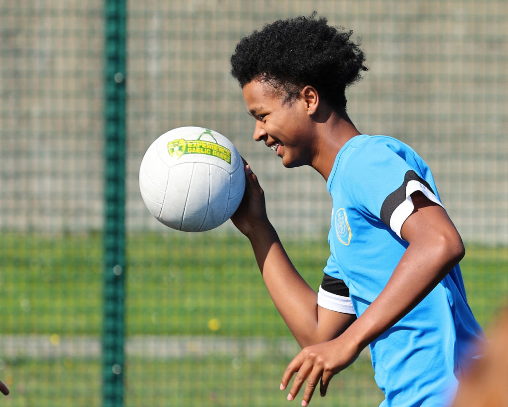 Smiling young player in a blue jersey practicing Gaelic football outdoors.