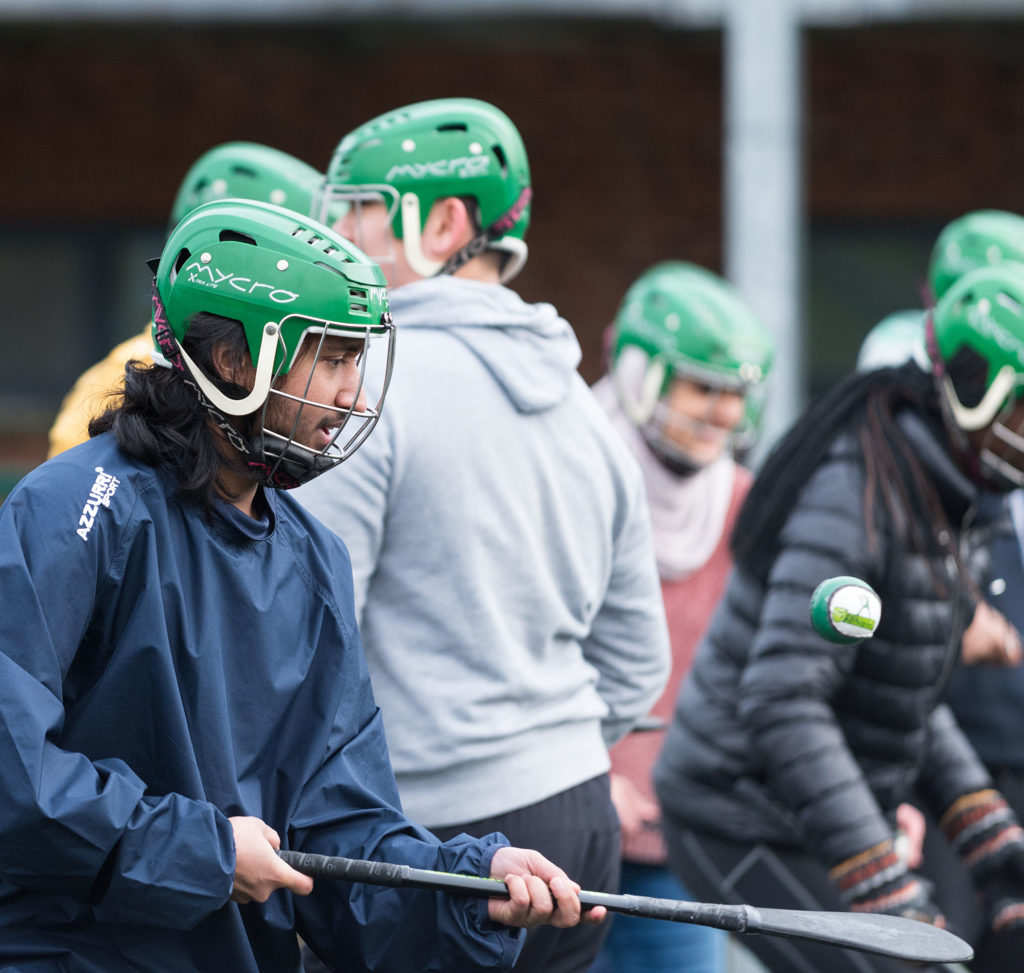 People playing hurling, wearing green helmets and focusing on a sliotar during practice.