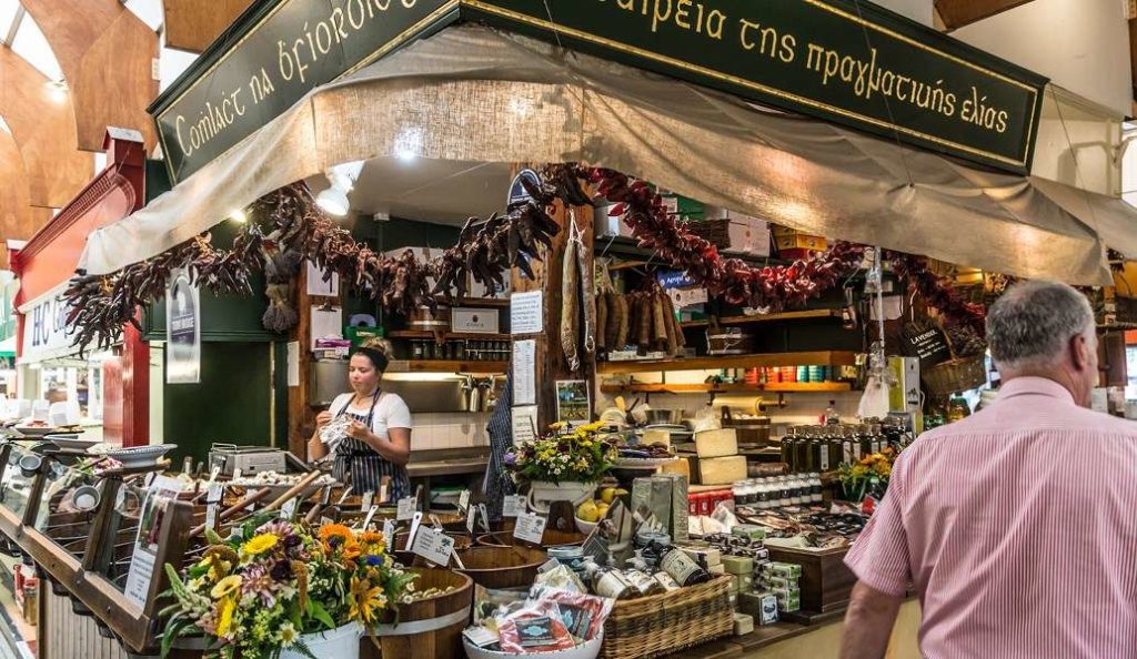 Busy market stall selling local produce, spices, and flowers with a vendor assisting customers.