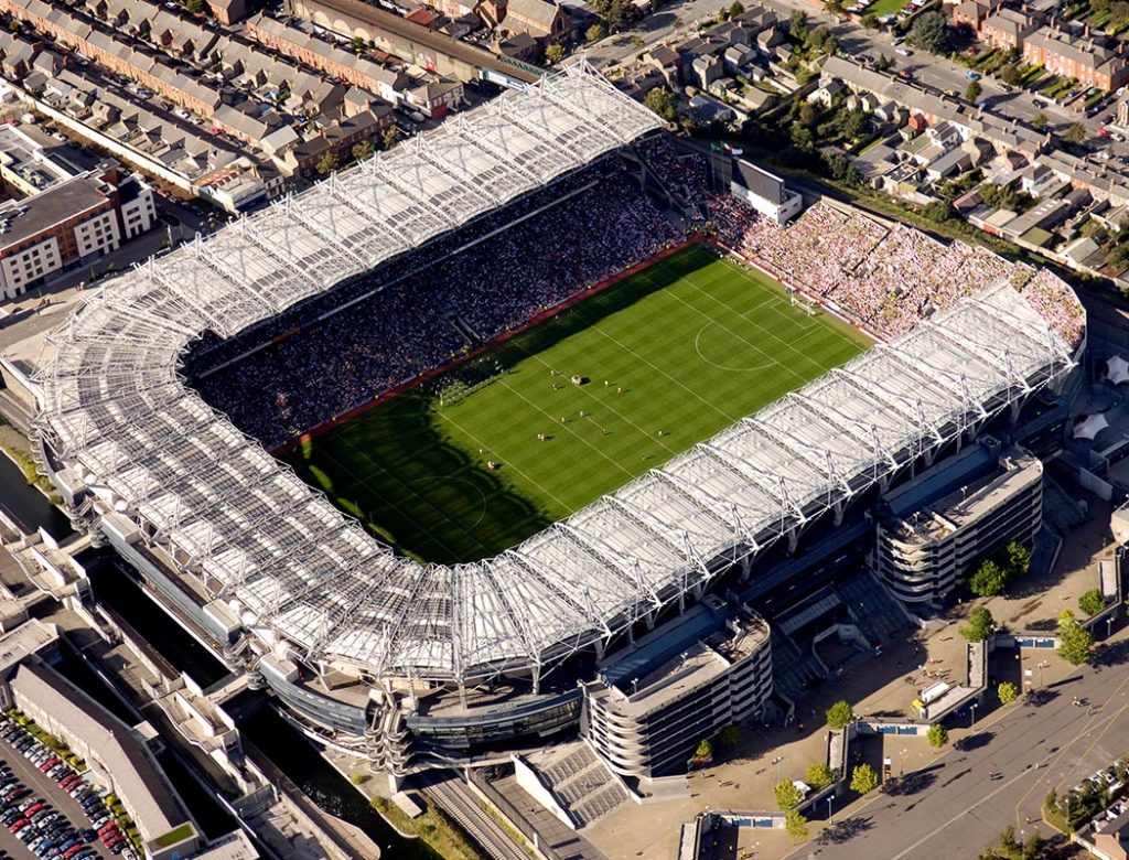 Aerial view of a sports stadium filled with spectators, surrounded by urban buildings, during a daytime event.