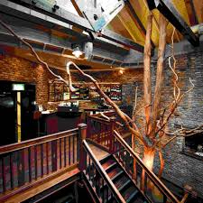 Rustic interior with exposed beams, brick walls, and a tree sculpture near a wooden staircase and seating area.